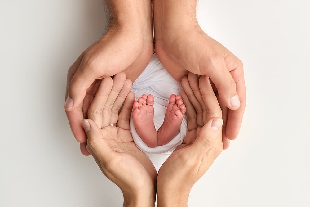 A newborn's feet cradled in two parents' hands